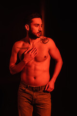 Fototapeta na wymiar Muscular man touching chest on black background with red lighting