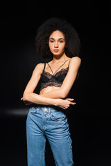 Sensual african american woman in jeans and bra looking at camera on black background