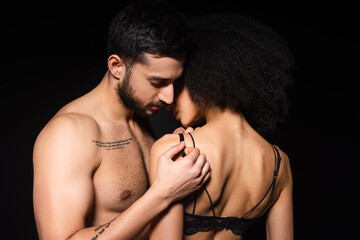 Tattooed man undressing african american woman isolated on black