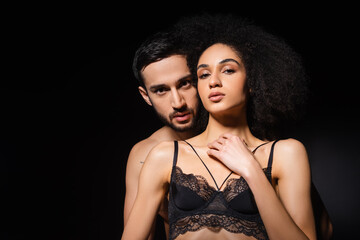 Sexy interracial couple looking at camera isolated on black