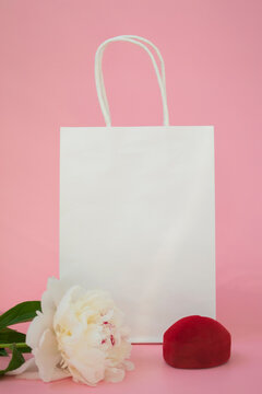 Gift white eco bag with copy space on a colored background with a white beautiful peony and a velvet box for decoration. Gift concept. Vertical photo