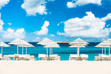 (Selective focus) Stunning view of some white thatch umbrellas and sunbeds on a white sand beach bathed by a beautiful, turquoise sea. Romazzino Beach, Porto Cervo, Sardinia, Italy.