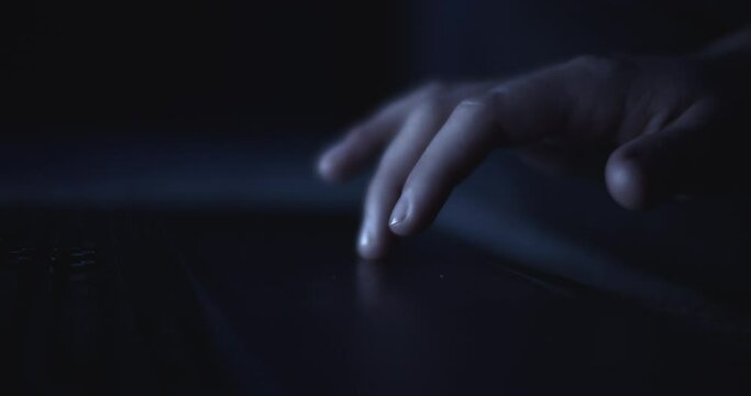 Hand scrolling a laptop's touchpad to search the internet at night. Slow motion, shallow depth of field, close up. 