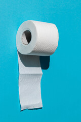 roll of a white toilet paper isolated on a blue background close-up. hard shadows from the sun at noon