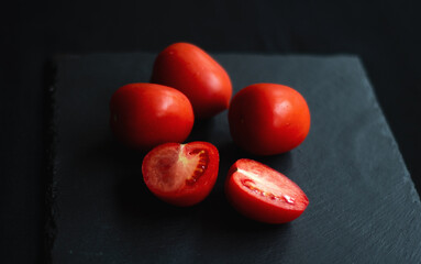 group of tomatoes, one cut in half, rests on a black board