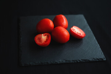 group of tomatoes, one cut in half, rests on a black board