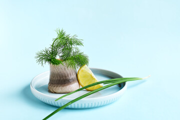 Herring fillet rolled up with lemon slice and dill on the plate on light blue background. Minimal...