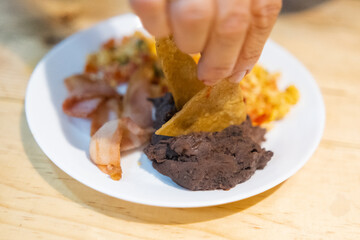 Hand picking tortilla chip from a Mexican-style eggs, bacon, and beans dish