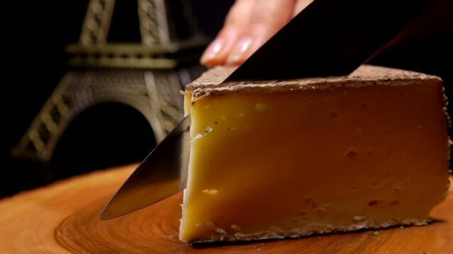 Close-up of the knife cutting a thin slice of the hard cheese on a wooden board