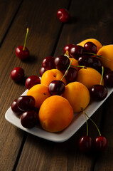 Fresh berries in a plate on a wooden table, low key. Apricot and sweet cherry fruits.