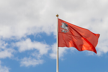 Flag of the Moscow region against the background of the cloudy sky. Red banner with the image of Saint George. The flag on the pole flutters in the wind. Copy space