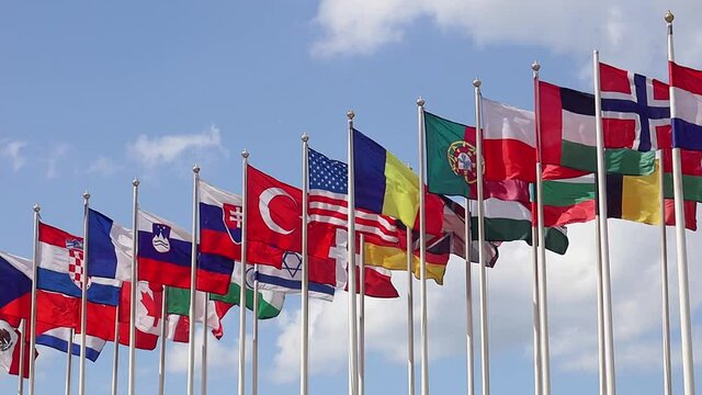 Group of flags of various states - as a symbol of world cooperation. Flags of the countries of the world on flagpoles flutter in the wind against the background of a blue sky