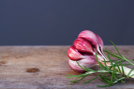 Pink garlic bulb and green rosemary on a wooden board  close up. Food ingredients on the table with copy space.