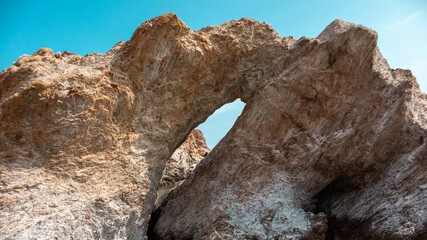 Big rock with a hole on wild mediterranean sea shore with blue sky. Travel Greece near Athens. Summer nature scenic lagoon