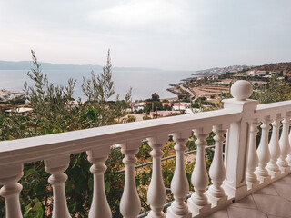 Traditional Greek architecture white terrace balcony with balusters. View on gray cloudscape and Aegean sea coast. Summer scenic view from country house near Athens, Greece