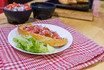 Mexican mollete and lettuce on a plate above white and red checkered napkin