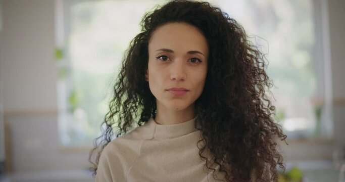 Portrait of a beautiful young woman with curly hair looking at the camera. Close up, slow motion. 