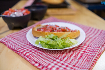 Mexican mollete and lettuce on a plate above white and red checkered napkin