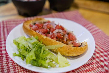 Mexican mollete and lettuce on a plate above white and red checkered napkin