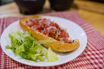 Mexican mollete and lettuce on a plate above white and red checkered napkin
