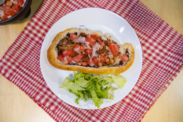Mexican mollete and lettuce on a plate above white and red checkered napkin