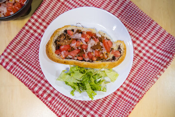 Mexican mollete and lettuce on a plate above white and red checkered napkin