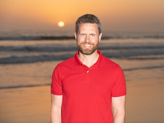 cheerful man with beard in sunset over sea. happy unshaven guy on beach background.