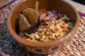 Mexican-style eggs, bacon, and refried beans with tortilla chips in clay bowl