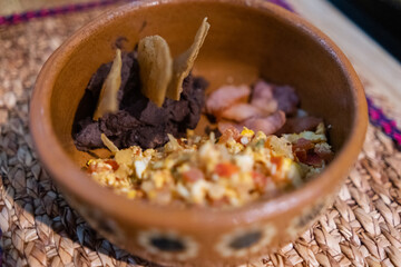 Mexican-style eggs, bacon, and refried beans with tortilla chips in clay bowl