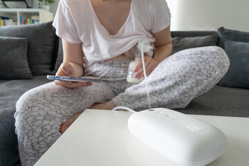 Close up on midsection of unknown caucasian woman holding baby bottle and breast pump pumping milk...