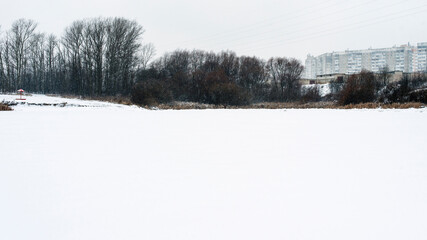 Winter urban Russian landscape, high-rise buildings, trees and a frozen pond covered with snow