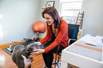 Woman sitting at desk in home office petting her pet pitbull dog