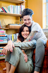 Portrait of happy woman sitting on chair hugging wife sitting on floor