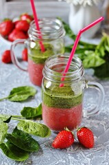 Two-layered smoothies made of strawberries and spinach in a trendy jar with a handle. Next to fresh strawberries and juicy spinach leaves. organic food. For vegan and raw food nutrition. 