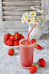 strawberry smoothie in a clear glass with a straw. Next to fresh strawberries. Useful dietary and organic food. For vegan and raw food nutrition. Light background. Soft focus.