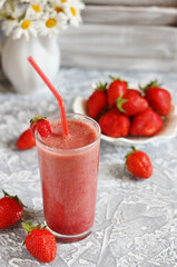 strawberry smoothie in a clear glass with a straw. Next to fresh strawberries. Useful dietary and organic food. For vegan and raw food nutrition. Light background. Soft focus.