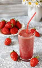 strawberry smoothie in a clear glass with a straw. Next to fresh strawberries. Useful dietary and organic food. For vegan and raw food nutrition. Light background. Soft focus.