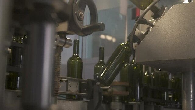 Slow-motion Automatic conveyor with moving bottles on belt, in the foreground the bottle is filled with wine. Automated wine bottling production line. Industrial machines at the wine bottling factory