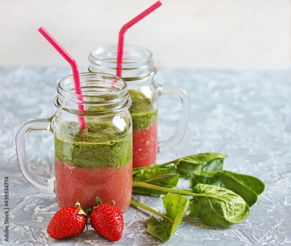 Wall mural Two-layered smoothies made of strawberries and spinach in a trendy jar with a handle. Next to fresh strawberries and juicy spinach leaves. organic food. For vegan and raw food nutrition. 