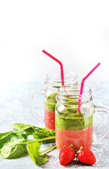 Two-layered smoothies made of strawberries and spinach in a trendy jar with a handle. Next to fresh strawberries and juicy spinach leaves. organic food. For vegan and raw food nutrition. 