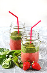 Two-layered smoothies made of strawberries and spinach in a trendy jar with a handle. Next to fresh strawberries and juicy spinach leaves. organic food. For vegan and raw food nutrition. 