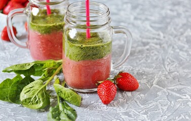 Two-layered smoothies made of strawberries and spinach in a trendy jar with a handle. Next to fresh strawberries and juicy spinach leaves. organic food. For vegan and raw food nutrition. 