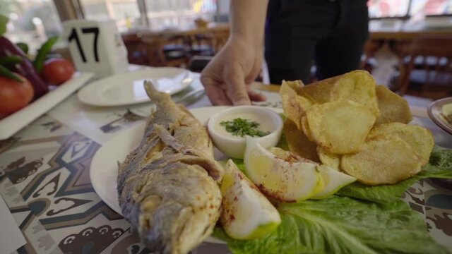 Serving a dish of roasted sea bream fish with potatoes and sauce