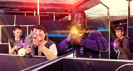 Portrait of young man and woman with laser pistols playing laser tag on dark labyrinth