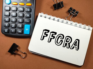 Business concept.Text FFCRA on notebook with calculator and paper clips on gray background.