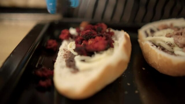Blue tongs adding chopped meat to traditional Mexican molletes above black tray