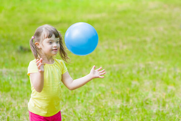 Young girl with syndrome down plays with a ball in a summer park