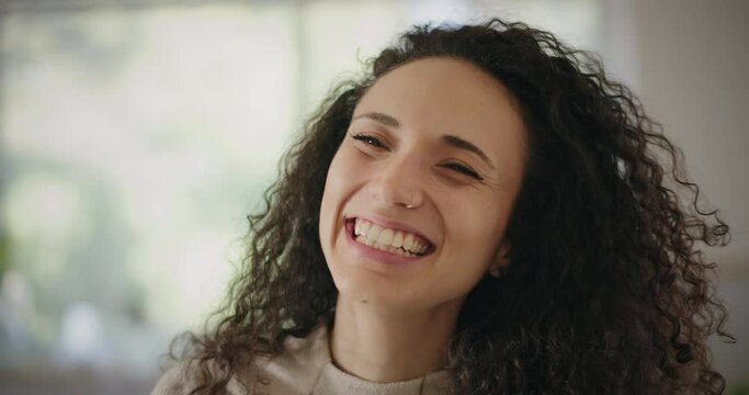 Portrait of a beautiful happy young woman with curly hair laughing while looking to the camera. Close up, slow motion. 