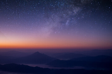 Milky way is visible in the dark night sky. Beautiful starry background with galaxy nebula and beautiful view of foggy landscape on top of mountain at the morning.