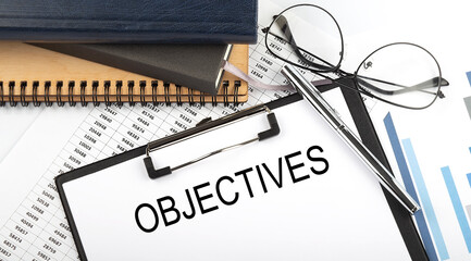 Text OBJECTIVES on Office desk table with notebooks, supplies,analysis chart, on the white...